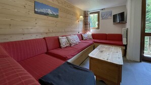 A cozy room with a red sofa, a wooden table, and a TV. - Stylish Duplex with Mezzanine for 7, Steps from Slopes (Les Menuires)