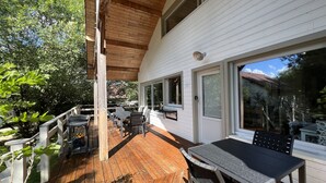 A covered outdoor patio with wooden flooring, a table and chairs, and a view of a white building with large windows. - The clock Chalain 2 (Doucier)