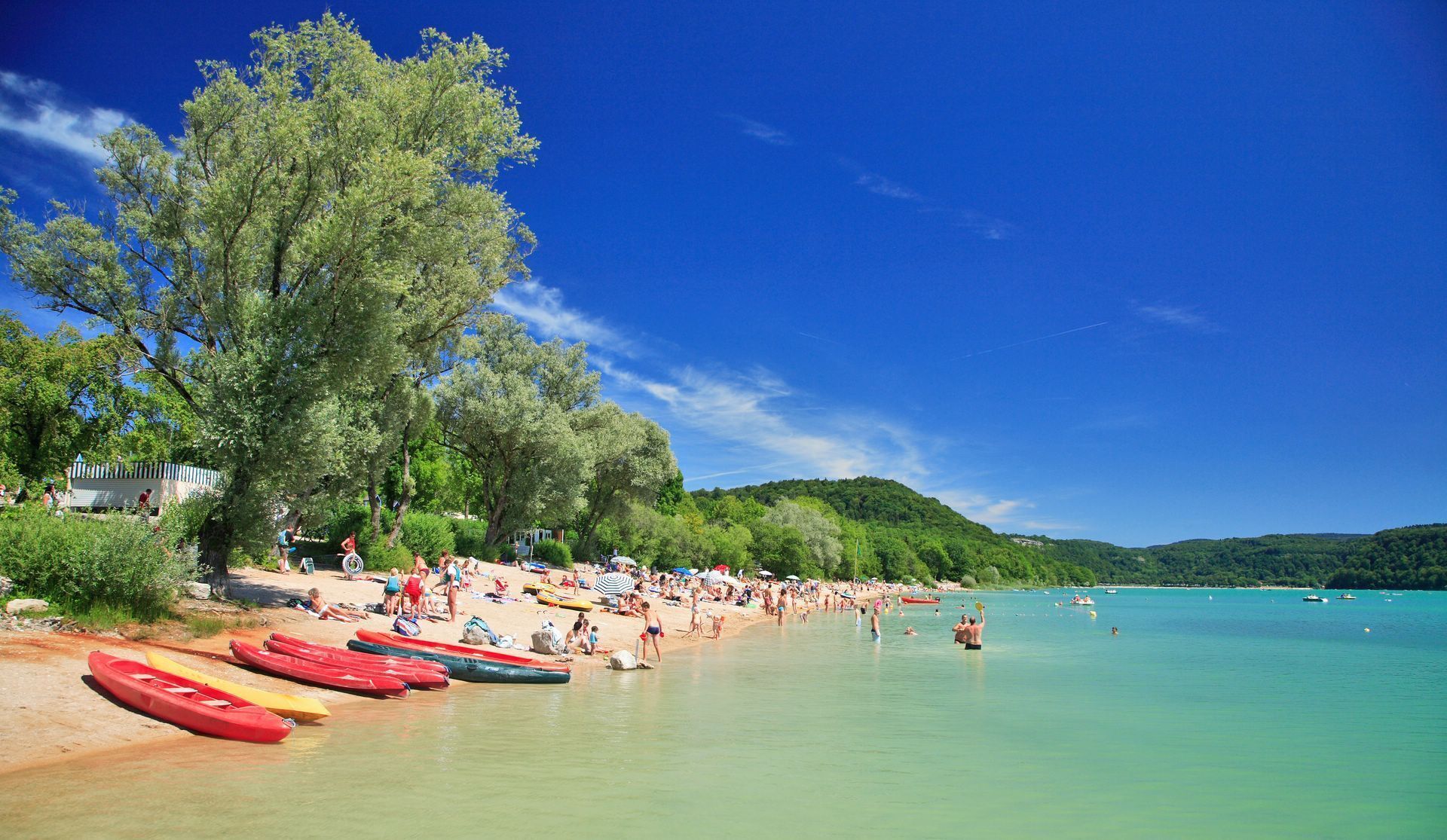 A beach with kayaks lined up on the sand, people sunbathing, and boats in the water. - The clock Chalain 2 (Doucier)