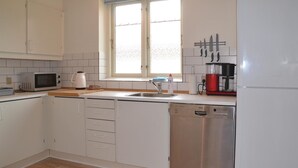 A compact kitchen with white cabinets, a stainless steel dishwasher, a microwave, a kettle, and a coffee maker. - 1 bedroom cozy apartment in Varde (Varde)