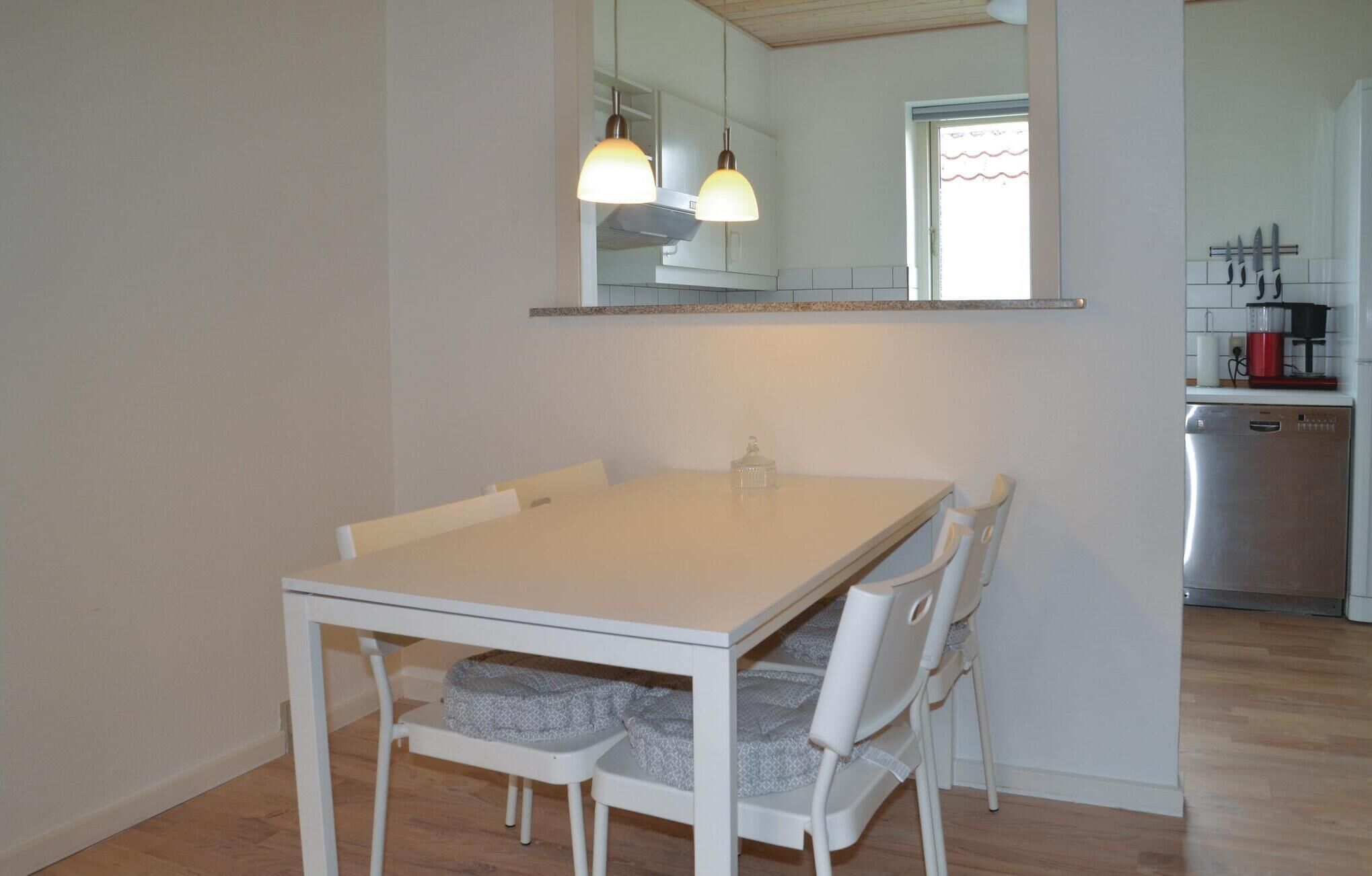 A dining area with a white table and chairs, a kitchen in the background, and a large mirror above the table.