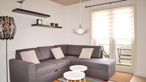 A modern living room with a grey sectional sofa, two white round tables, a colorful striped rug, a floor lamp, and a pendant light. - 1 bedroom cozy apartment in Varde (Varde)