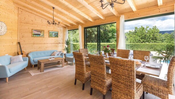 A wooden interior with a dining area, sofas, and a large window offering a view of greenery. - Amazing home in Kamenmost with sauna (Kamenmost)