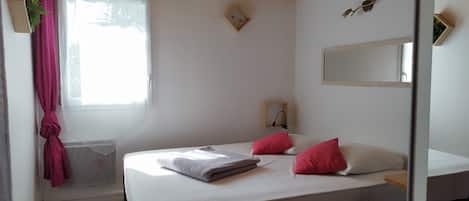 Un dormitorio con una cama, un ventanal con cortinas, un radiador, un espejo y techo de madera.