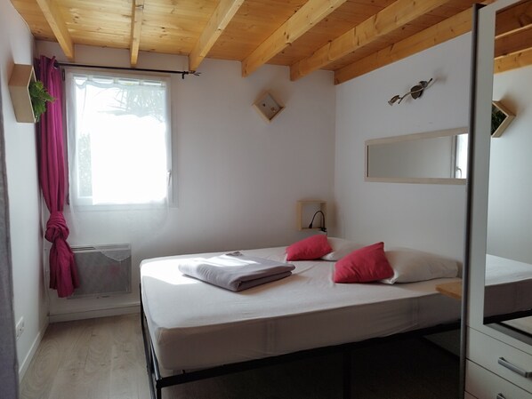 Quarto com cama, janela com cortinas, radiador, espelho e teto de madeira.
