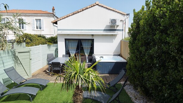 Un patio con una mesa, sillas, un jacuzzi y una pequeña palmera.