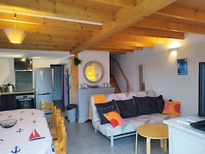 A cozy living room with a sofa, a small table, and a kitchen area with a refrigerator and stove.