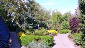A garden pathway with a curved brick design, surrounded by various shrubs and trees. - Here you will find harmony for the soul and body, garden & house are inviting (Damp)