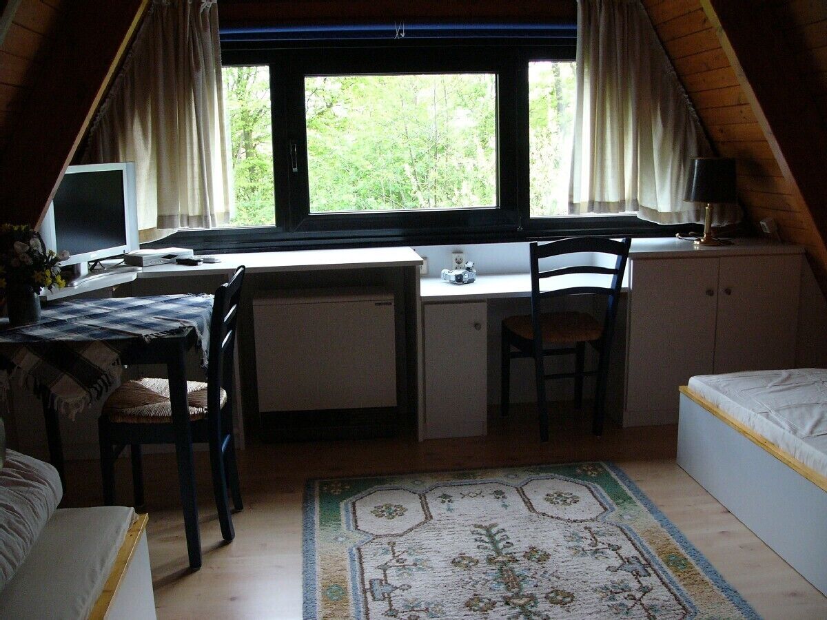 Ein kleiner, Dachzimmer-ähnlicher Raum mit Schreibtisch, Stuhl und Bett.