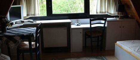 Ein kleiner, Dachzimmer-ähnlicher Raum mit Schreibtisch, Stuhl und Bett.