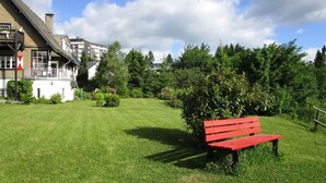 Un espace verdoyant avec un banc rouge, un bâtiment doté d’un toit en pente et une végétation luxuriante en arrière-plan.