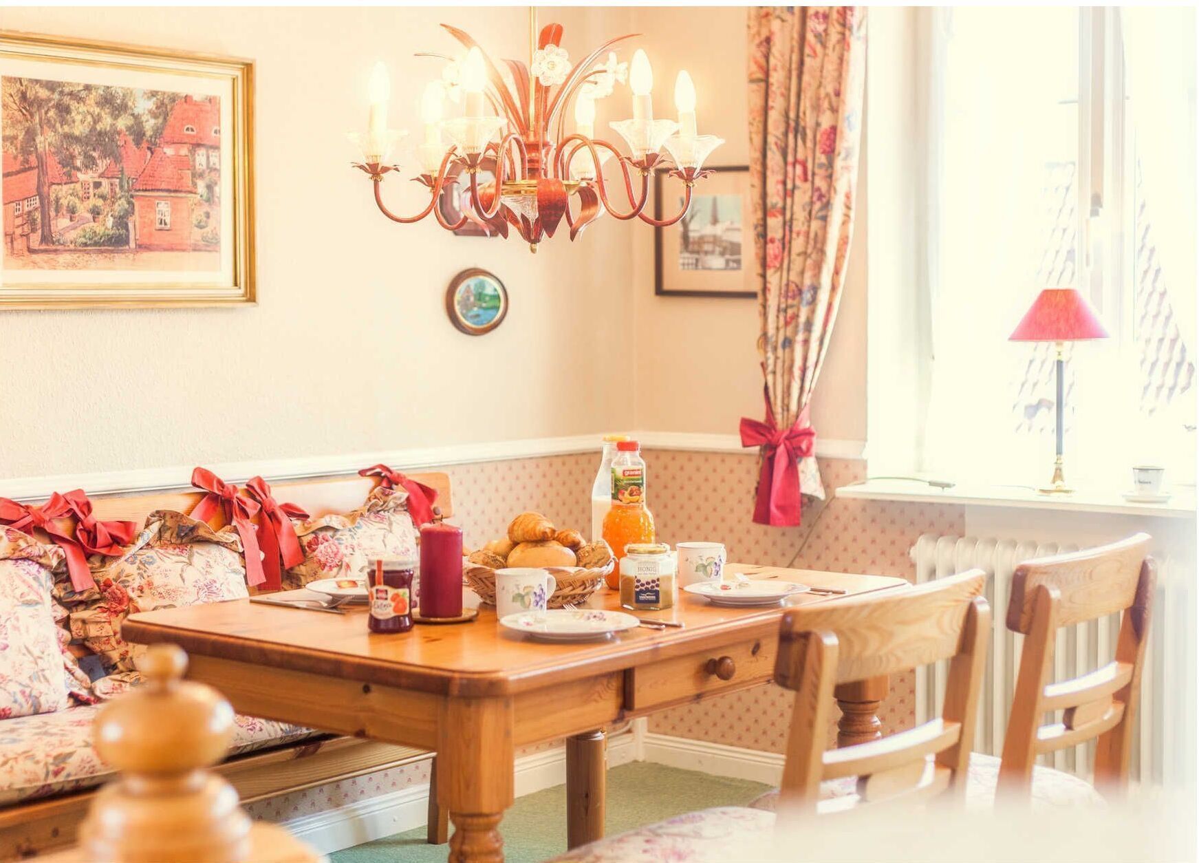 A dining area with a wooden table set for breakfast, featuring pastries, a bottle of orange juice, and a candle.