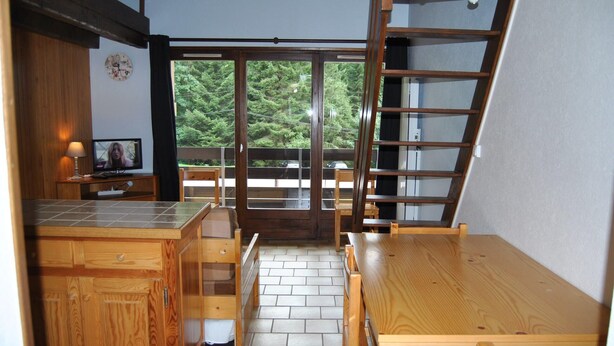 A compact kitchen with wooden cabinets, a tiled floor, a wooden table, and a television.