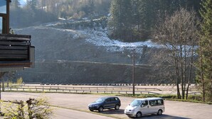 A parking area with two cars, a building with a balcony, and a mountainous landscape in the background.