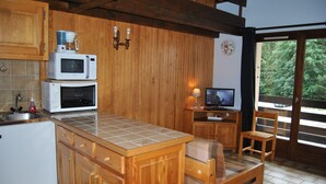A kitchen with wooden cabinets, a microwave, an oven, and a small dining area with a table and chairs.