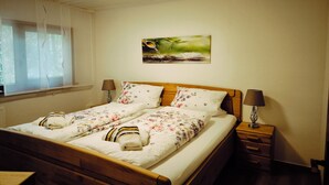 Una cama bien hecha con ropa de cama floral, una lámpara de noche y un cuadro en la pared.