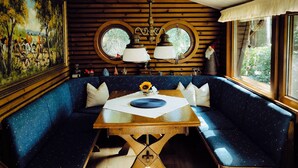 Un cuarto acogedor con techo de madera, un cuadro grande a la izquierda, un espejo redondo sobre un sofá azul y una mesa con un jarrón de flores.