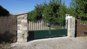 Ein verschlossener Eingang mit einer Steinmauer und einem Metallgitter, umgeben von Bäumen und blauem Himmel.