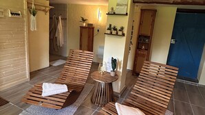 A spa room with wooden loungers, a small round table, and a wall-mounted shelf with plants. - Farmhouse near the Baltic Sea (Upahl)
