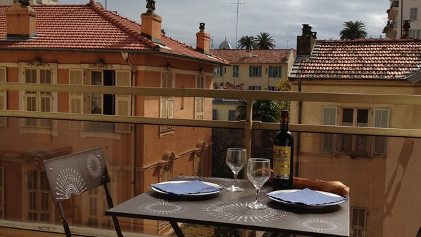 A balcony with a table set for two, overlooking a cityscape with red-tiled buildings. - Bright, quiet and centrally located apartment with balcony and air conditioning (Nice)