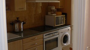 A compact kitchen with wooden cabinets, a microwave, a stove, and a washing machine. - Bright, quiet and centrally located apartment with balcony and air conditioning (Nice)