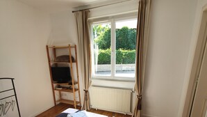 Ein Schlafzimmer mit einem großen Bett, einem Fenster mit Vorhängen, einem Heizkörper und einer Holzleiter.