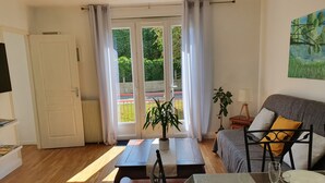Ein Wohnzimmer mit einer Couch, einem Esstisch für zwei Personen und einer Glastür, die auf einen Balkon führt.