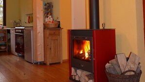 Una habitación acogedora con estufa de leña, piso de madera y una zona de cocina con lavavajillas y alacenas.