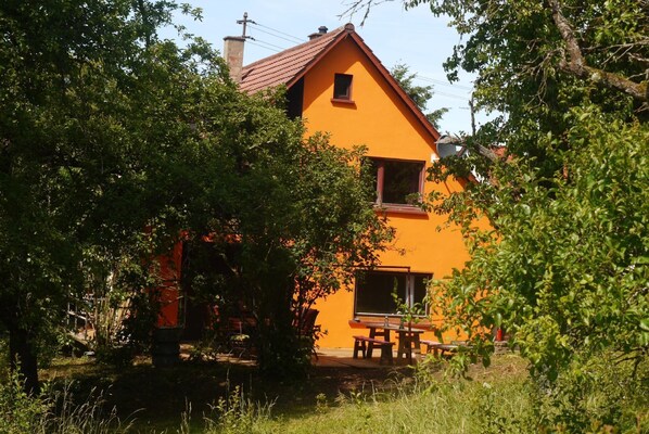 Una casa con techo rojo y paredes anaranjadas, rodeada de árboles.
