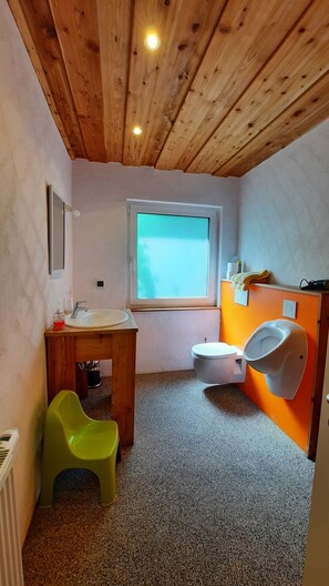 Un baño pequeño con techo de madera, una ventana, un lavabo, un inodoro y una silla verde.