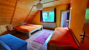 Un dormitorio en el ático, acogedor, con dos camas de madera, un sofá azul y un amplio ventanal con vistas a la vegetación.