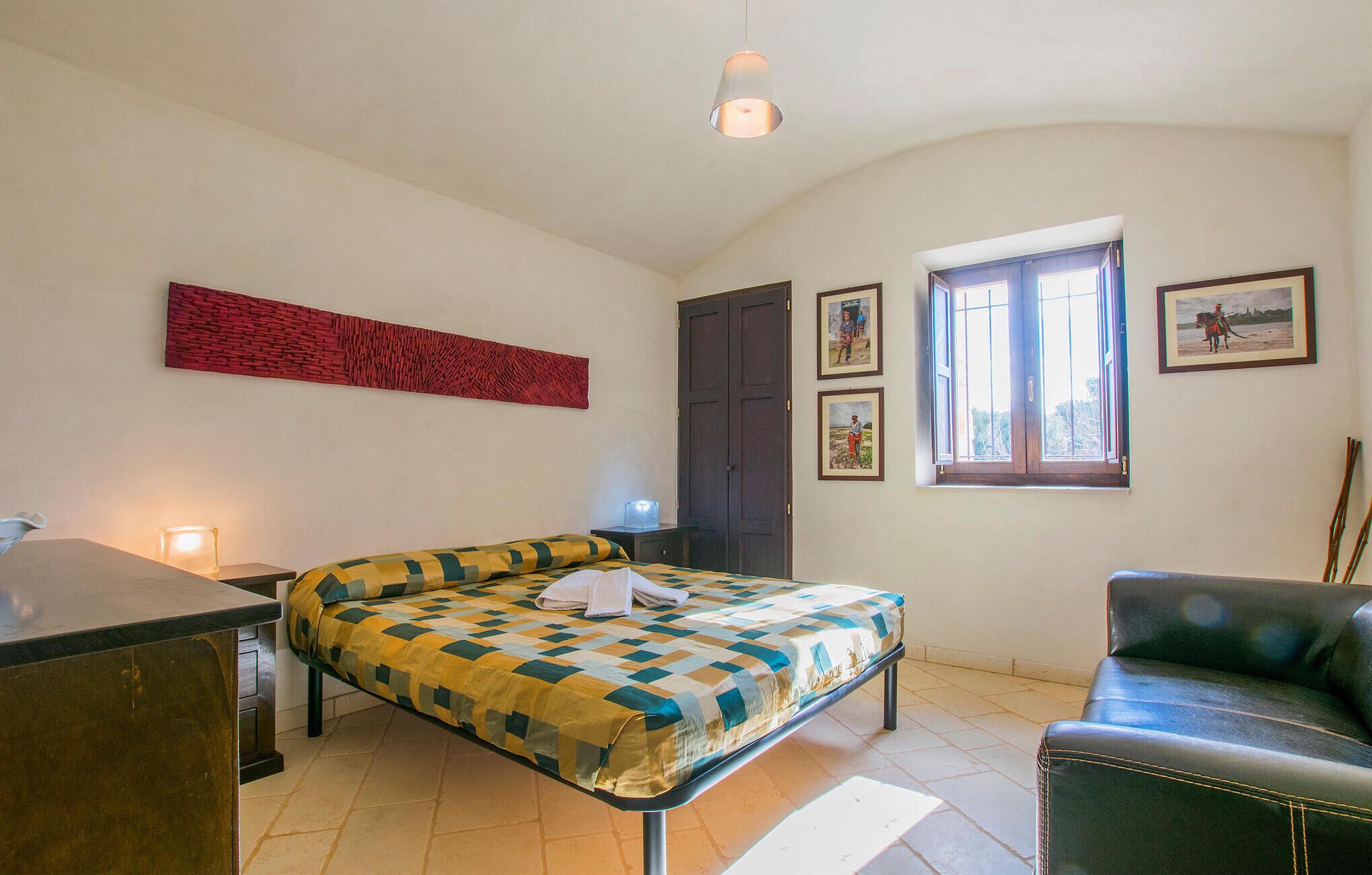 A bedroom with a bed, a desk, a chair, a window, and artwork on the walls.