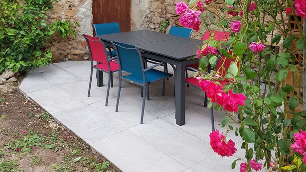 Un edificio in pietra con una porta di legno e una finestra. Si nota un tavolo con sedie e una pianta in vaso con fiori rosa.