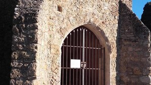 Un edificio in pietra con una croce in cima, un ingresso sbarrato e gradini che conducono ad esso.