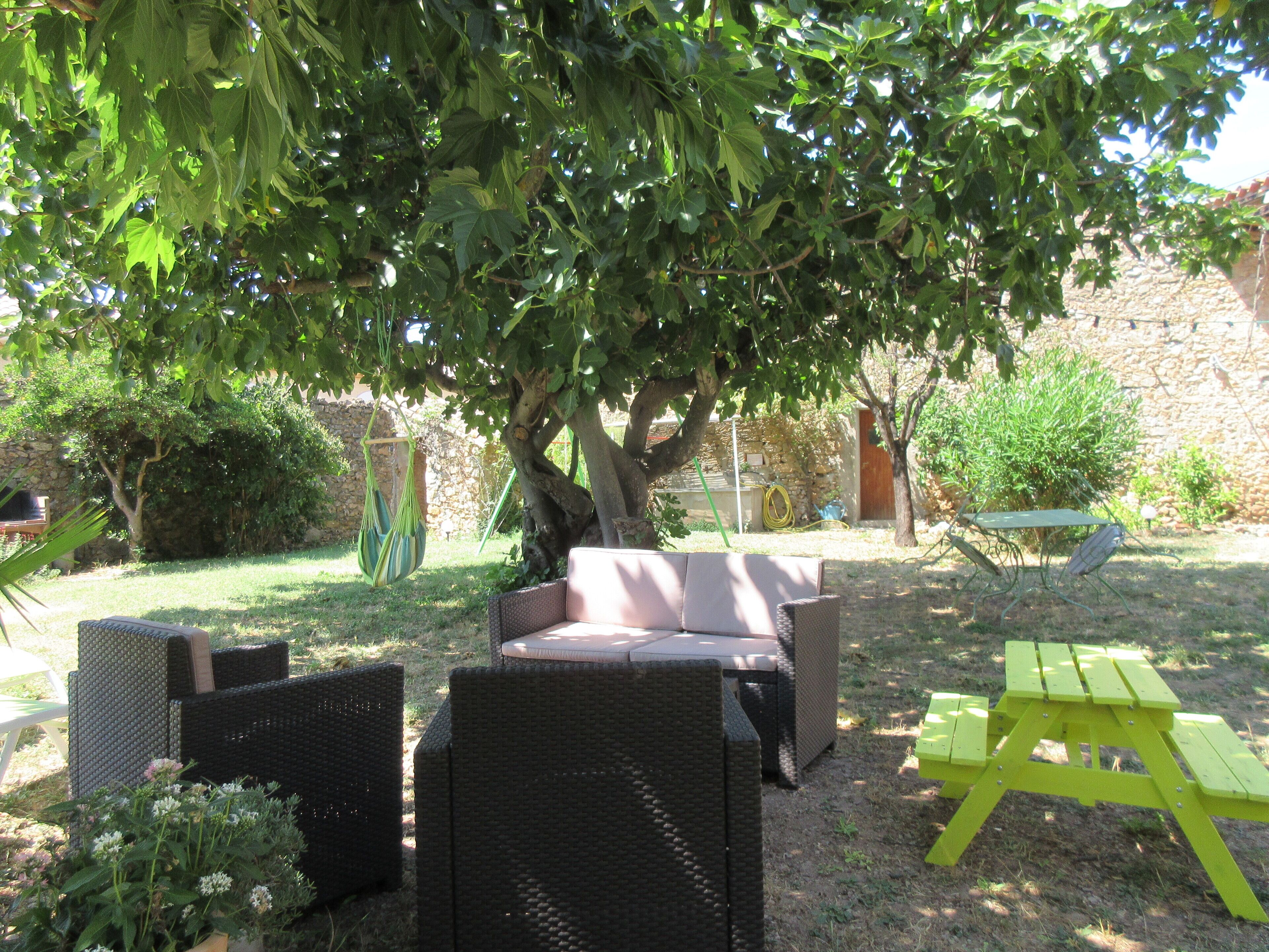 An outdoor seating area with wicker furniture under a tree, a stone wall, and a green picnic table.