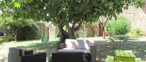 An outdoor seating area with wicker furniture under a tree, a stone wall, and a green picnic table.
