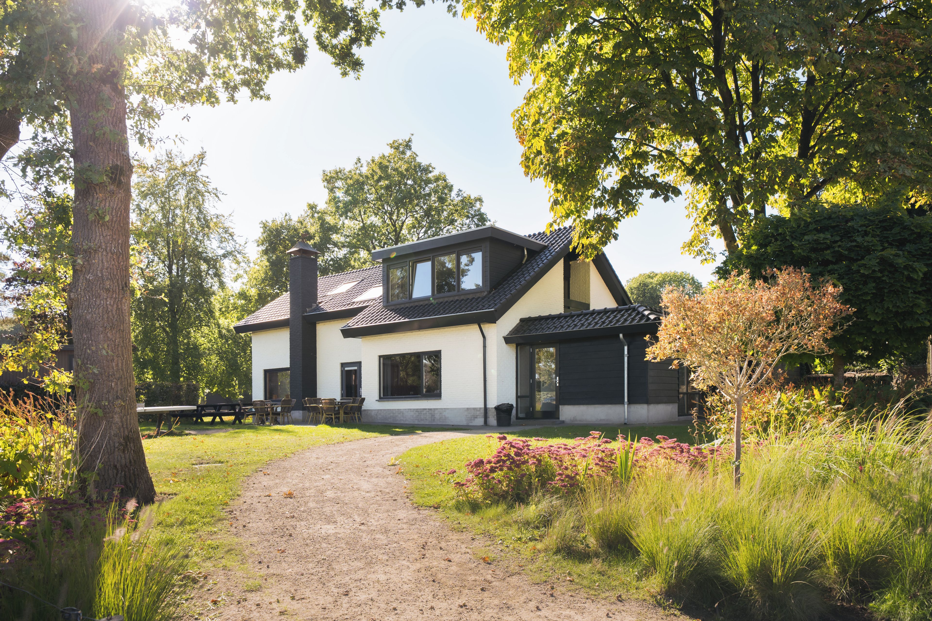A two-story house with a dirt path leading to the entrance, surrounded by greenery and trees.