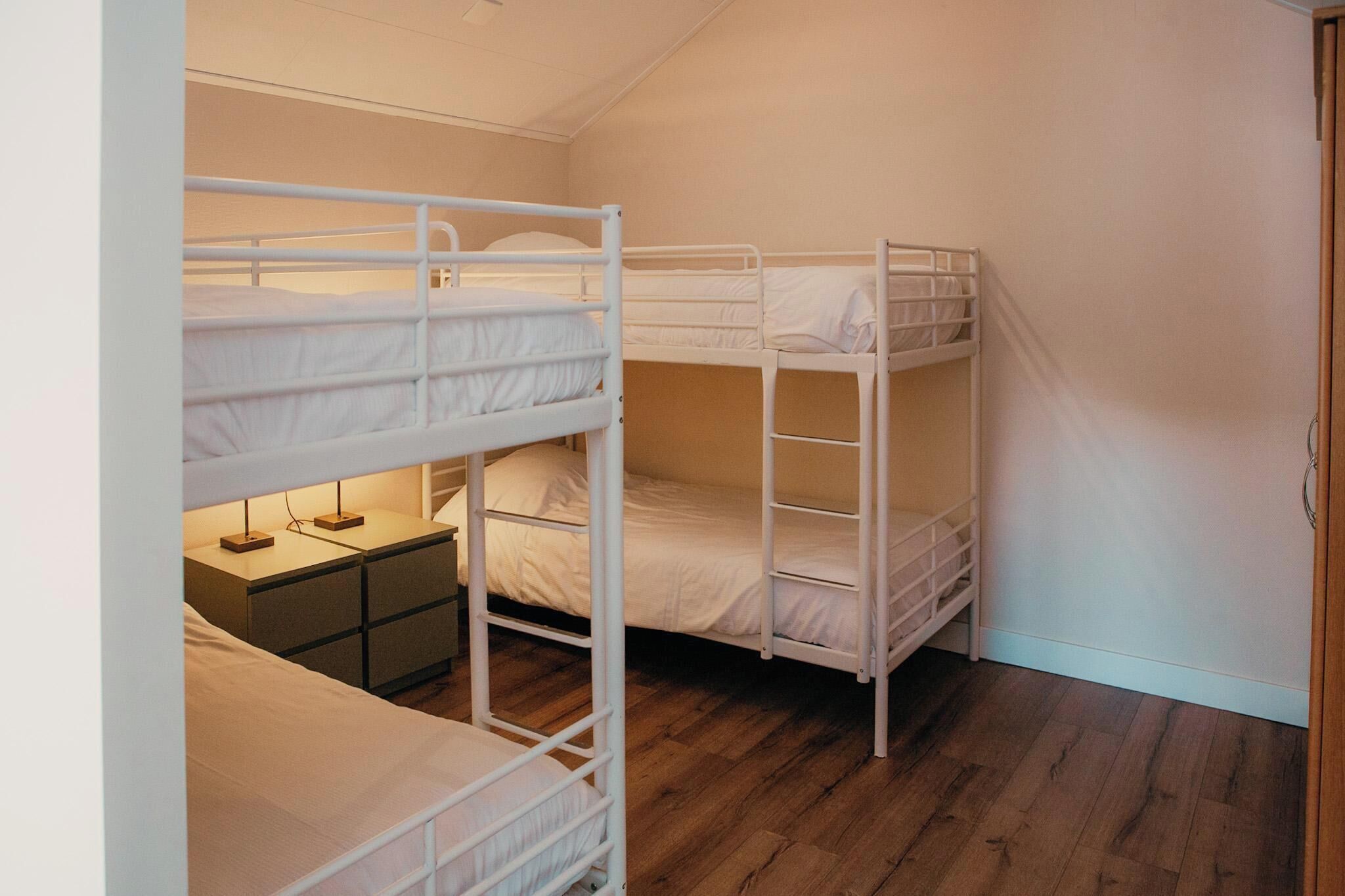 Een kamer met drie stapelbedden, een klein nachtkastje en een houten vloer.