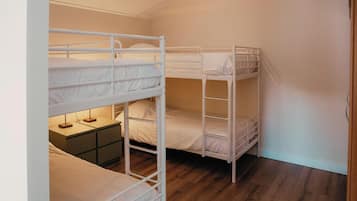 Een kamer met drie stapelbedden, een klein nachtkastje en een houten vloer.