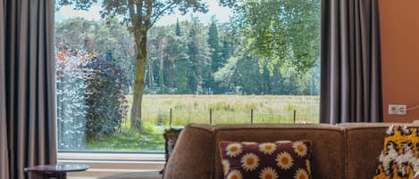 Een woonkamer met een groot raam, een bruine bank en een kleine tafel.
