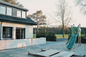 A modern house with a patio, a slide, and a playground.