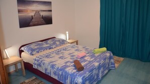 Une chambre à coucher avec un lit, une table de chevet, une lampe, un tableau au mur et une fenêtre avec des rideaux.