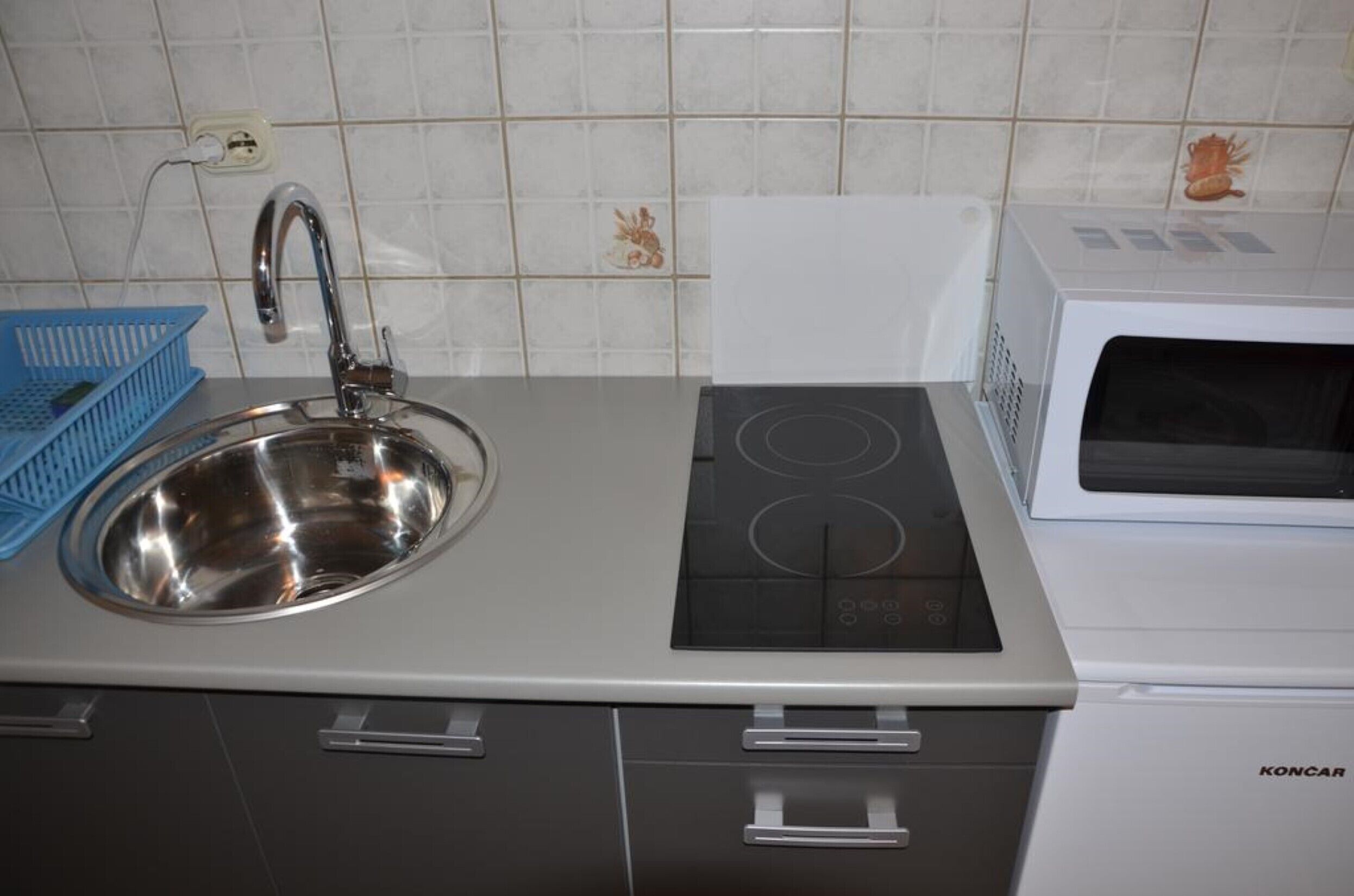 A kitchen with a stainless steel sink, a built-in stovetop, and a white microwave.