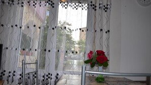 Une pièce comprenant une table, une chaise, une chaise en métal, un vase avec des fleurs et une fenêtre avec un rideau.