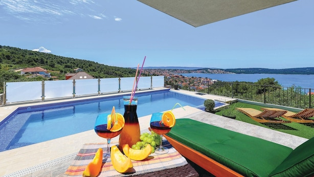 A pool with a view of a lake and hills, a table with drinks and fruit, and a green cushioned area. - Gorgeous home in Trogir with sauna (Trogir)
