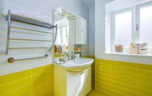 Un baño con una decoración en tonos amarillo y blanco, un lavamanos, un espejo y un perchero para toallas.
