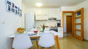 Cozinha compacta com armários brancos, geladeira e área de refeições com duas cadeiras e uma mesa posta para dois.
