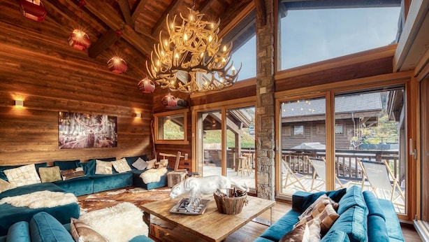 Un interior de cabaña acogedor con un sofá azul grande, una mesa de centro de madera y una araña.