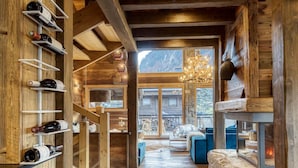 Un interior de madera con una estantería para vinos, una chimenea de piedra y vistas a través de un ventanal grande.