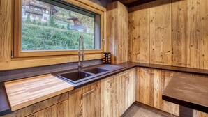 Una cocina con armarios de madera, un lavamanos doble y una ventana con vistas a un jardín.